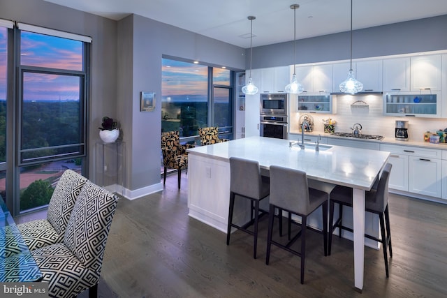 kitchen with appliances with stainless steel finishes, white cabinetry, sink, hanging light fixtures, and a center island with sink