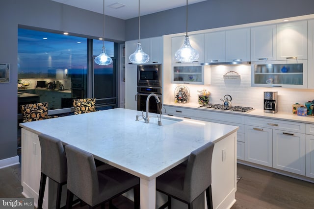 kitchen with a kitchen bar, white cabinetry, stainless steel gas cooktop, a kitchen island with sink, and light stone countertops