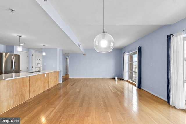 kitchen featuring sink, light hardwood / wood-style flooring, stainless steel fridge, and decorative light fixtures