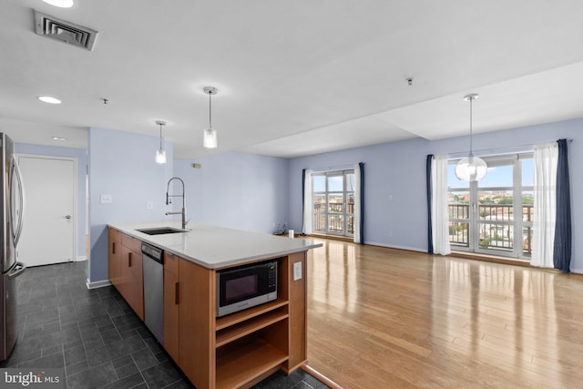 kitchen featuring appliances with stainless steel finishes, an island with sink, decorative light fixtures, and sink