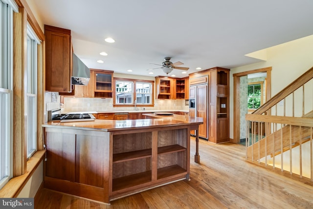 kitchen featuring kitchen peninsula, wall chimney exhaust hood, a healthy amount of sunlight, and light hardwood / wood-style floors