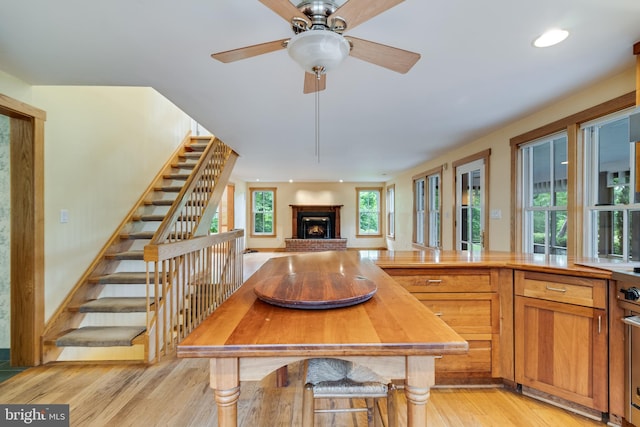 kitchen with ceiling fan, a fireplace, and light wood-type flooring