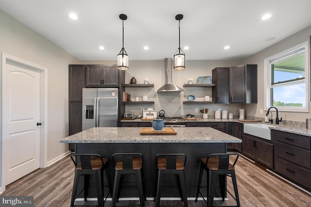 kitchen featuring dark brown cabinetry, sink, wall chimney exhaust hood, stainless steel appliances, and a kitchen island