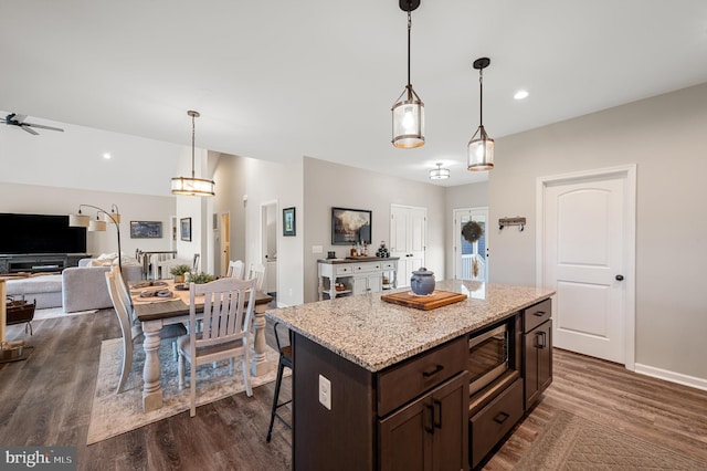 kitchen featuring a center island, stainless steel microwave, hanging light fixtures, ceiling fan, and dark brown cabinets