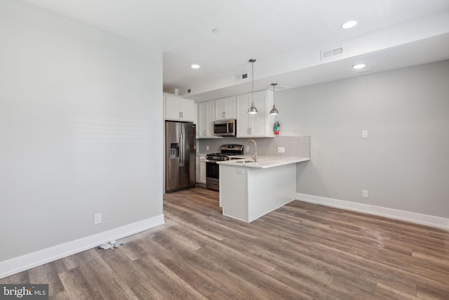 kitchen with wood-type flooring, stainless steel appliances, hanging light fixtures, white cabinets, and kitchen peninsula