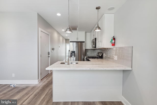 kitchen featuring appliances with stainless steel finishes, sink, kitchen peninsula, white cabinetry, and hardwood / wood-style flooring