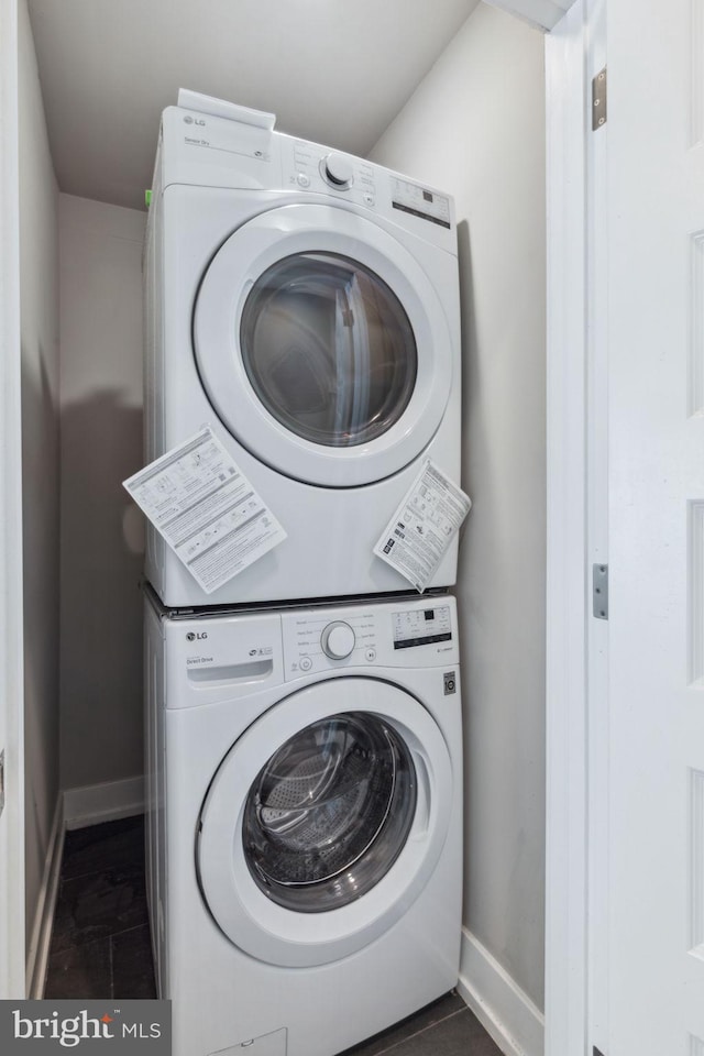 washroom with dark tile patterned floors and stacked washer / drying machine