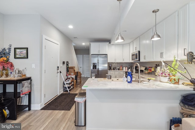 kitchen featuring stainless steel appliances, white cabinets, kitchen peninsula, decorative backsplash, and light wood-type flooring