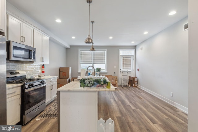 kitchen featuring white cabinets, a center island, stainless steel appliances, wood-type flooring, and decorative light fixtures