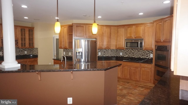 kitchen featuring dark stone counters, ornate columns, hanging light fixtures, and appliances with stainless steel finishes