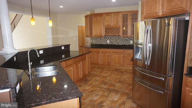 kitchen with stainless steel refrigerator with ice dispenser, tasteful backsplash, sink, dark stone countertops, and hanging light fixtures