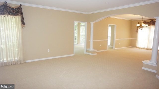 carpeted empty room featuring ornate columns, crown molding, and an inviting chandelier