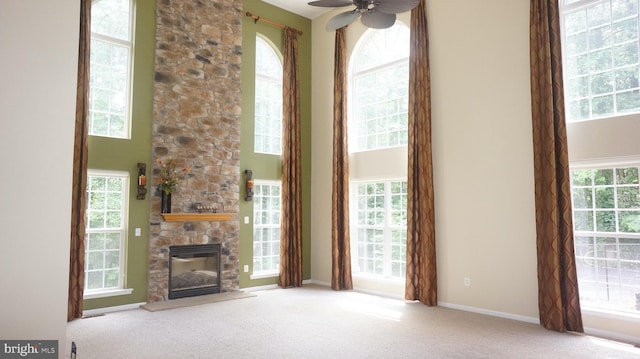 unfurnished living room with a wealth of natural light, a fireplace, a towering ceiling, and light colored carpet