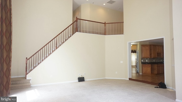 unfurnished living room featuring carpet flooring and a high ceiling