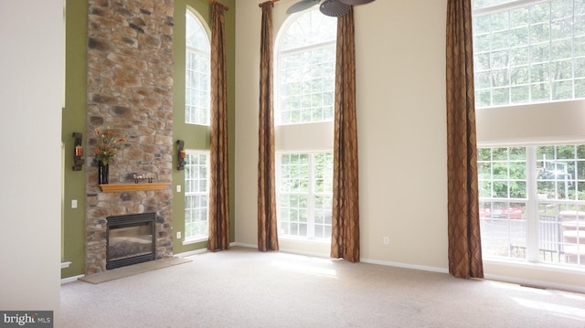 unfurnished living room featuring a stone fireplace, a towering ceiling, and light colored carpet