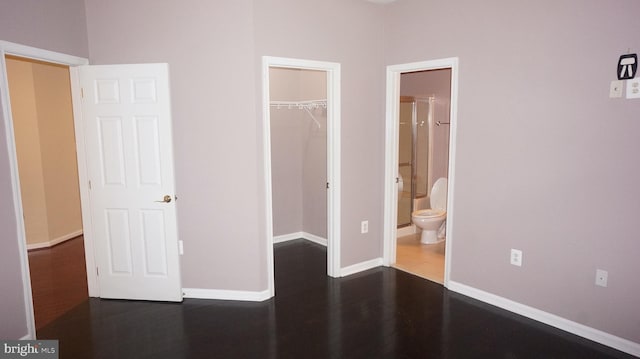 unfurnished bedroom featuring dark hardwood / wood-style floors, a spacious closet, connected bathroom, and a closet