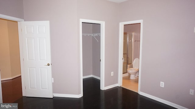 unfurnished bedroom featuring dark hardwood / wood-style flooring, a walk in closet, connected bathroom, and a closet