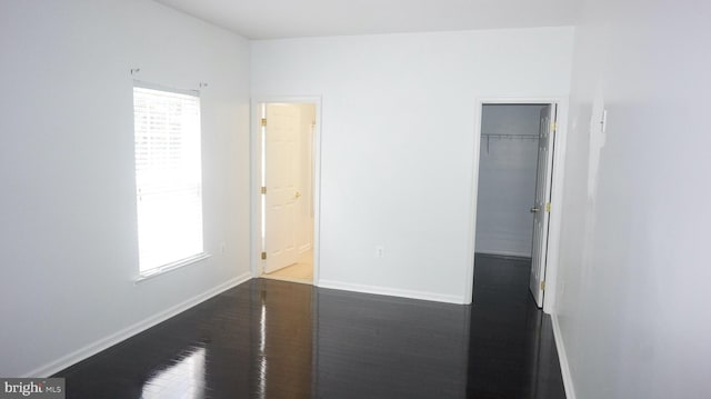 unfurnished bedroom featuring a walk in closet, dark hardwood / wood-style flooring, and a closet