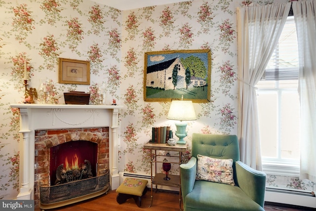 sitting room with hardwood / wood-style flooring, a brick fireplace, and a baseboard radiator