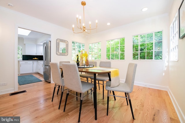 dining room featuring light wood-type flooring, ornamental molding, and an inviting chandelier