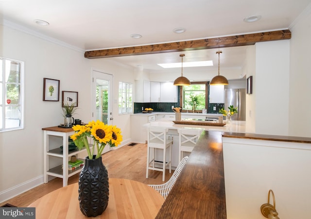 kitchen featuring backsplash, light hardwood / wood-style floors, white cabinetry, hanging light fixtures, and stainless steel refrigerator