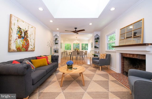 living room featuring a tile fireplace, ceiling fan, built in shelves, ornamental molding, and light wood-type flooring