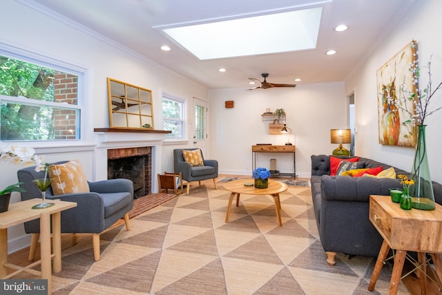 living room featuring a skylight, ceiling fan, a fireplace, and ornamental molding