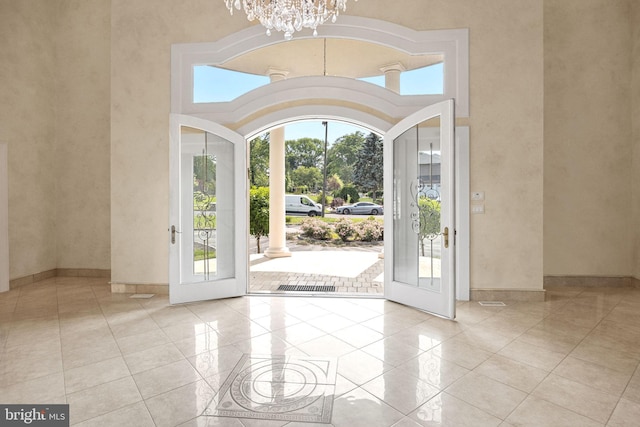 foyer entrance featuring french doors, a towering ceiling, a chandelier, and light tile patterned floors