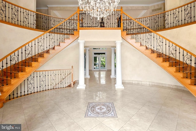 entryway with a chandelier, crown molding, a high ceiling, and decorative columns