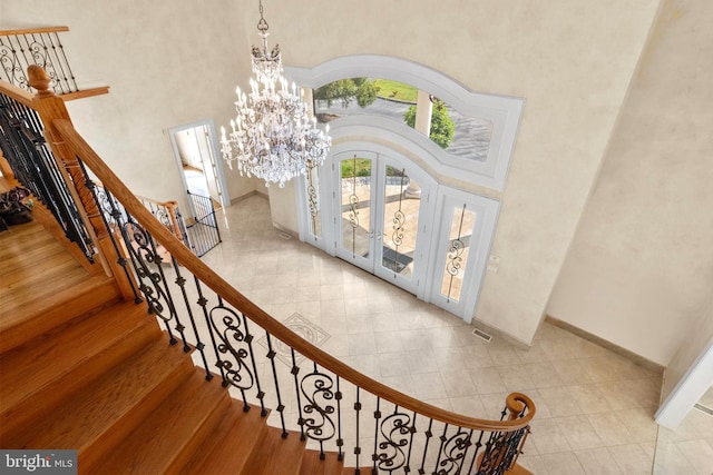 staircase with tile patterned flooring, a towering ceiling, and a chandelier