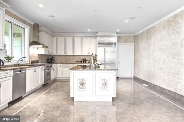 kitchen featuring a center island, wall chimney exhaust hood, crown molding, dark stone counters, and high quality appliances