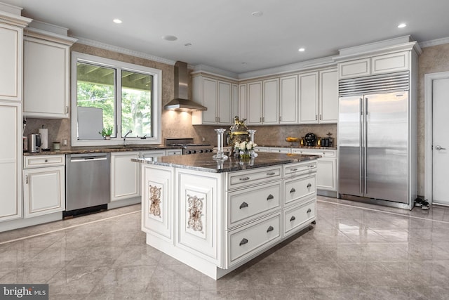 kitchen featuring a center island, stainless steel appliances, wall chimney range hood, dark stone countertops, and ornamental molding