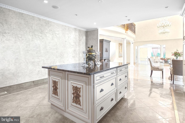 kitchen featuring ornate columns, ornamental molding, dark stone countertops, white cabinets, and a center island