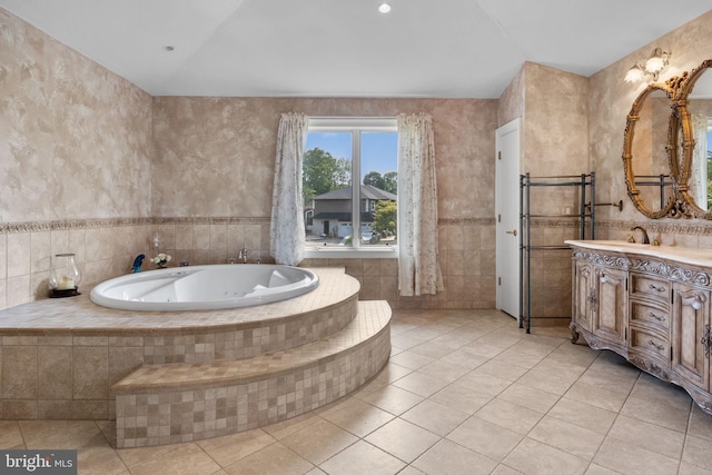 bathroom with tile patterned flooring, vanity, tile walls, and tiled bath