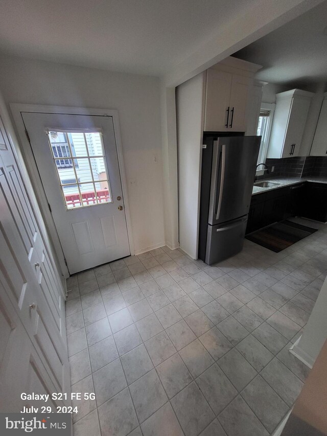 kitchen with light tile patterned floors, white cabinets, stainless steel fridge, and sink