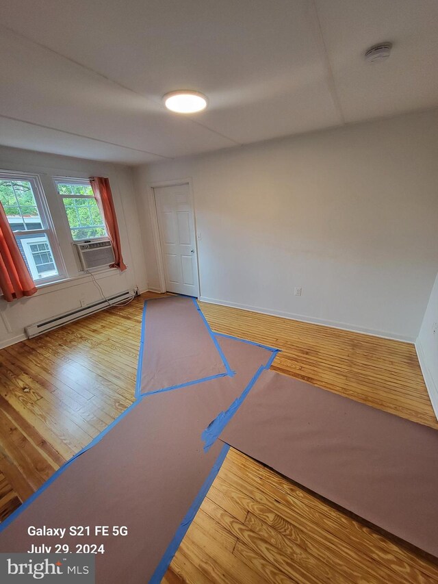 empty room with a baseboard heating unit, cooling unit, and wood-type flooring