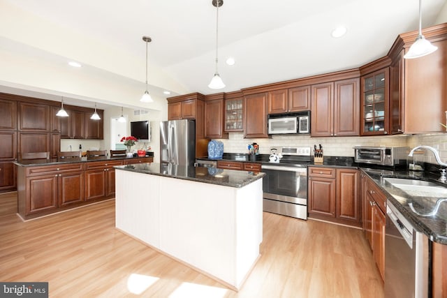 kitchen featuring light wood-style flooring, appliances with stainless steel finishes, a center island, a sink, and backsplash