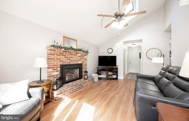 living area with ceiling fan, high vaulted ceiling, light wood-style flooring, baseboards, and a brick fireplace