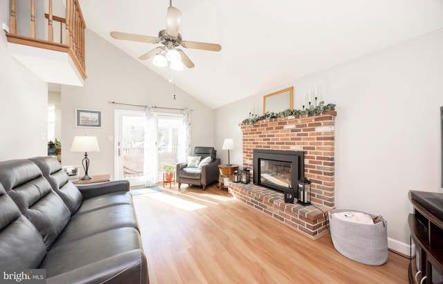 living room featuring baseboards, a ceiling fan, wood finished floors, a brick fireplace, and high vaulted ceiling