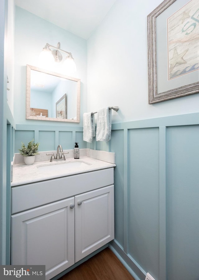 bathroom featuring wainscoting, a decorative wall, vanity, and wood finished floors