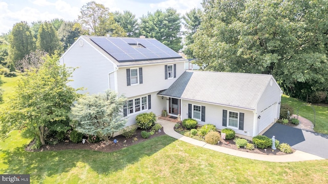 view of front of house featuring a garage, roof mounted solar panels, aphalt driveway, and a front yard