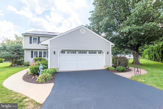 view of front of property with a garage, a front lawn, roof mounted solar panels, and aphalt driveway