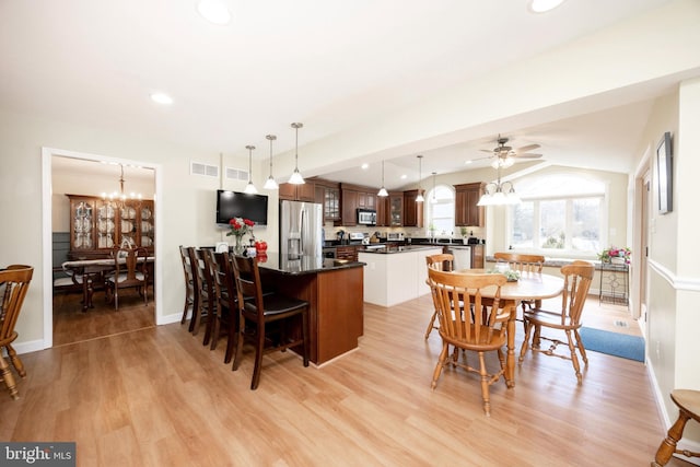 kitchen featuring stainless steel appliances, dark countertops, light wood-style floors, a peninsula, and a kitchen breakfast bar