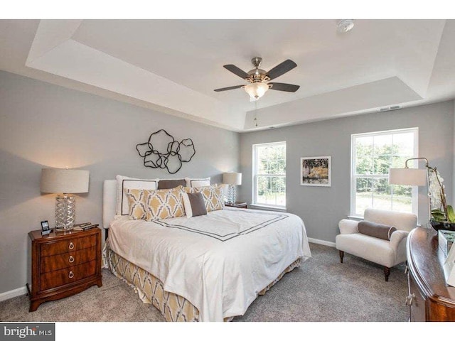 carpeted bedroom with a raised ceiling and ceiling fan