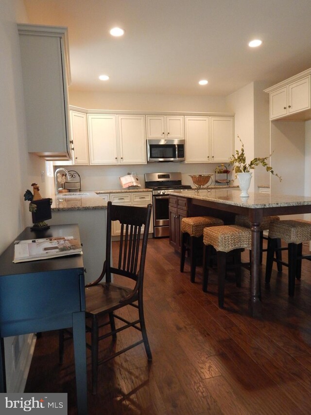 kitchen with light stone counters, dark hardwood / wood-style floors, stainless steel appliances, and white cabinets