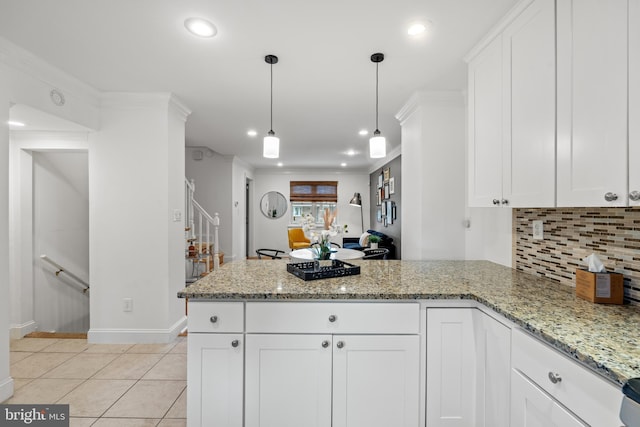 kitchen with light stone countertops, kitchen peninsula, white cabinetry, and hanging light fixtures