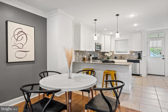 kitchen featuring kitchen peninsula, dark stone counters, stainless steel appliances, crown molding, and white cabinetry