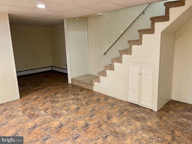 basement featuring a drop ceiling and a baseboard heating unit