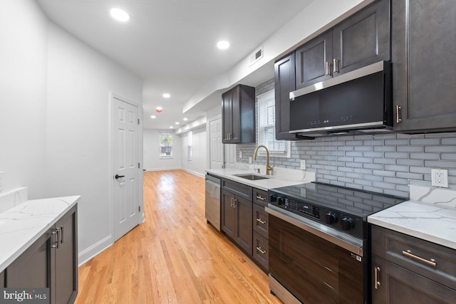 kitchen featuring tasteful backsplash, appliances with stainless steel finishes, sink, light hardwood / wood-style floors, and light stone counters