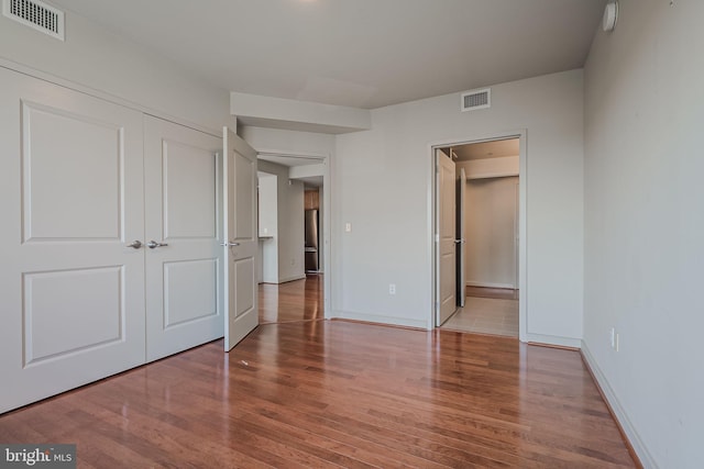 unfurnished bedroom featuring a closet, visible vents, wood finished floors, and baseboards